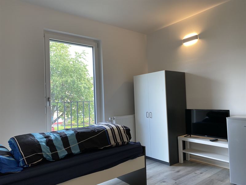 Zimmer mit Bett, Kleiderschrank, Fernseher und Kühlschrank